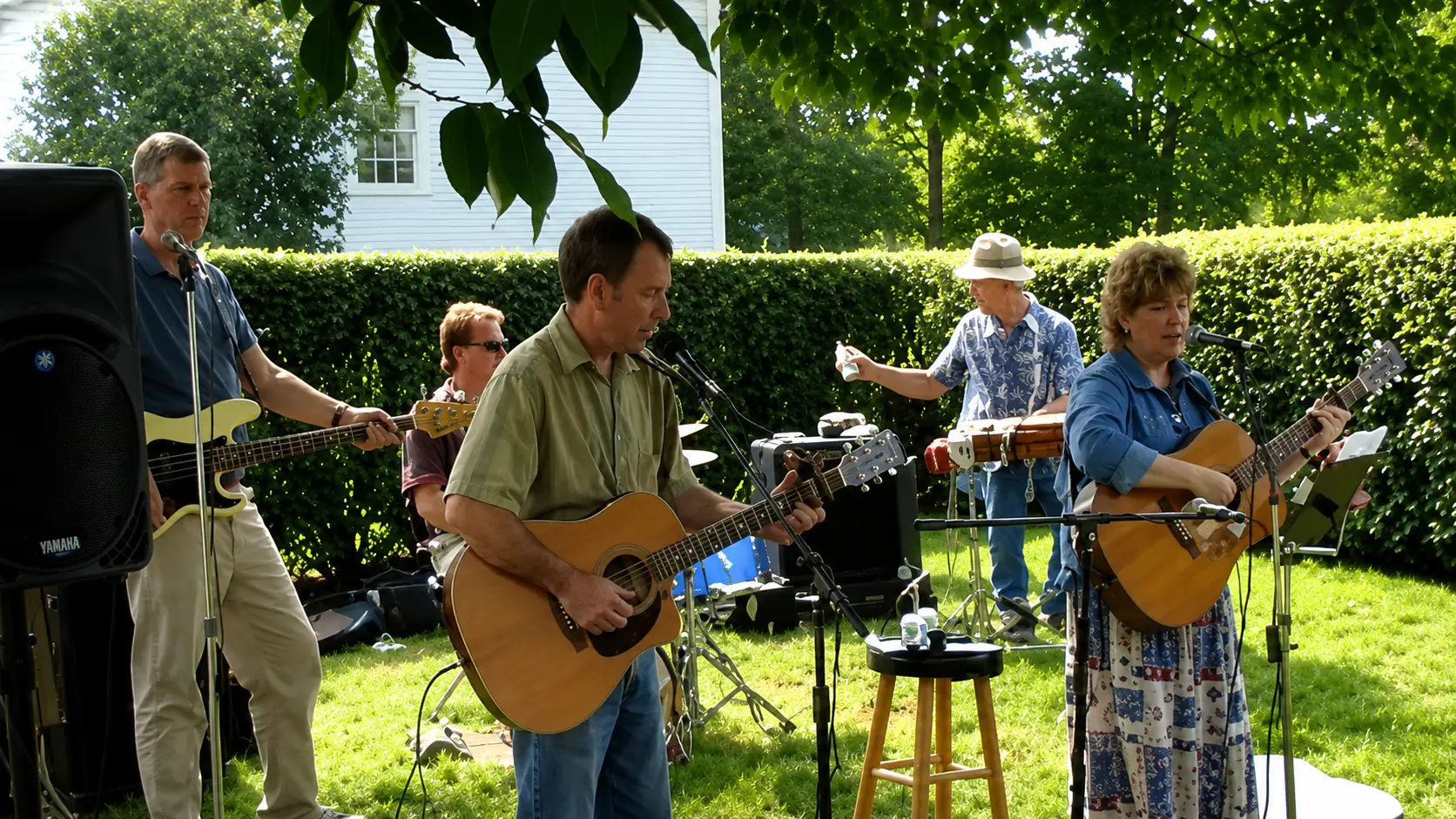 Musicians playing acoustic guitars and drums in a sunny backyard